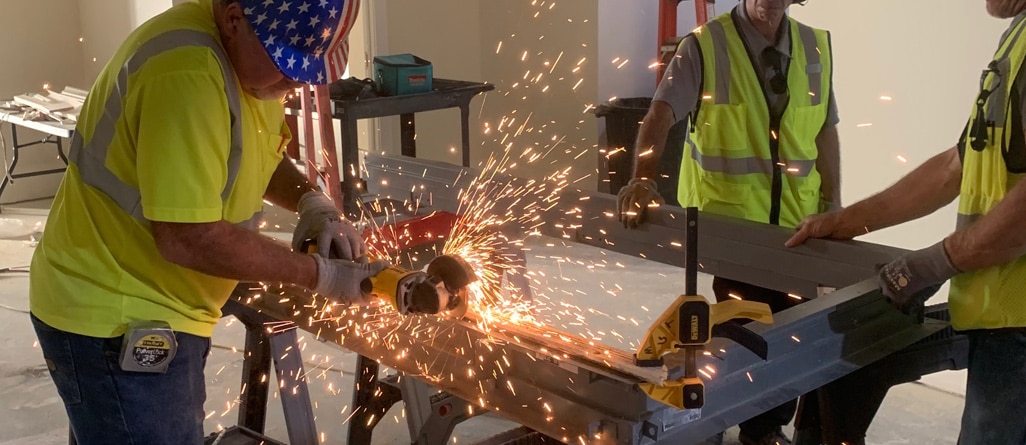 Picture of person in American flag hard hat using saw with sparks flying as two other people look on