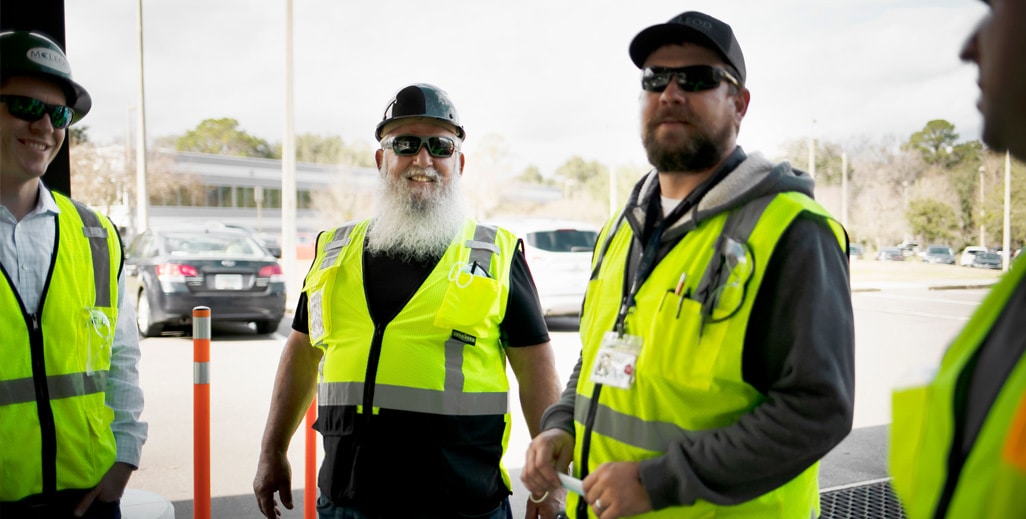 4 people in hats and vests talking with one slightly out of frame